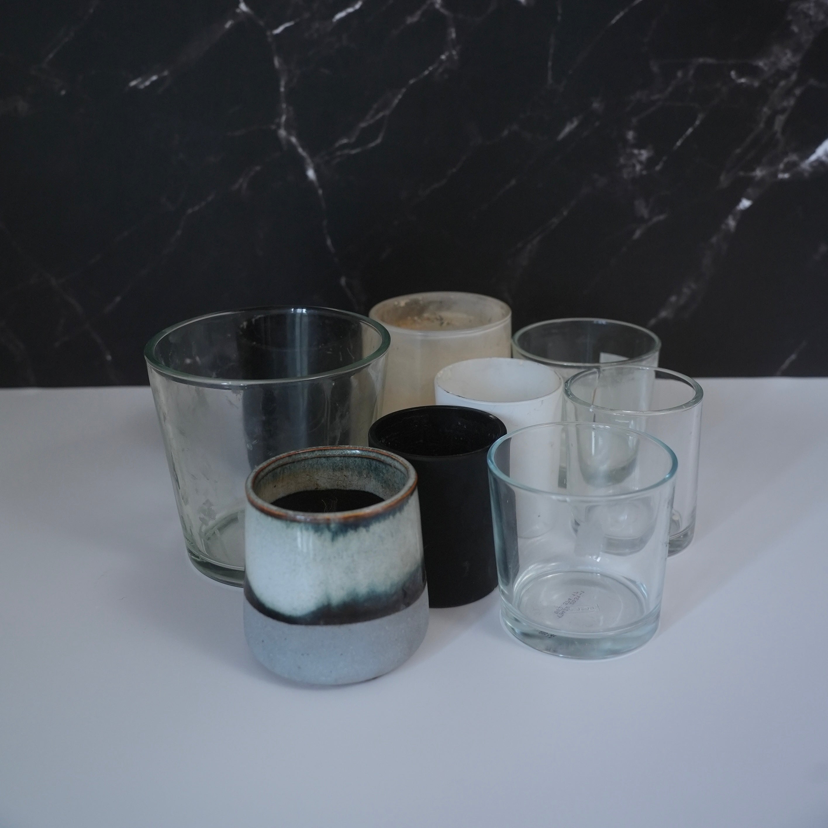 9 empty candle jars on a white bench top with marbled backdrop. 