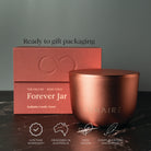 Rose gold candle vessel with packaging on a dark surface and green background