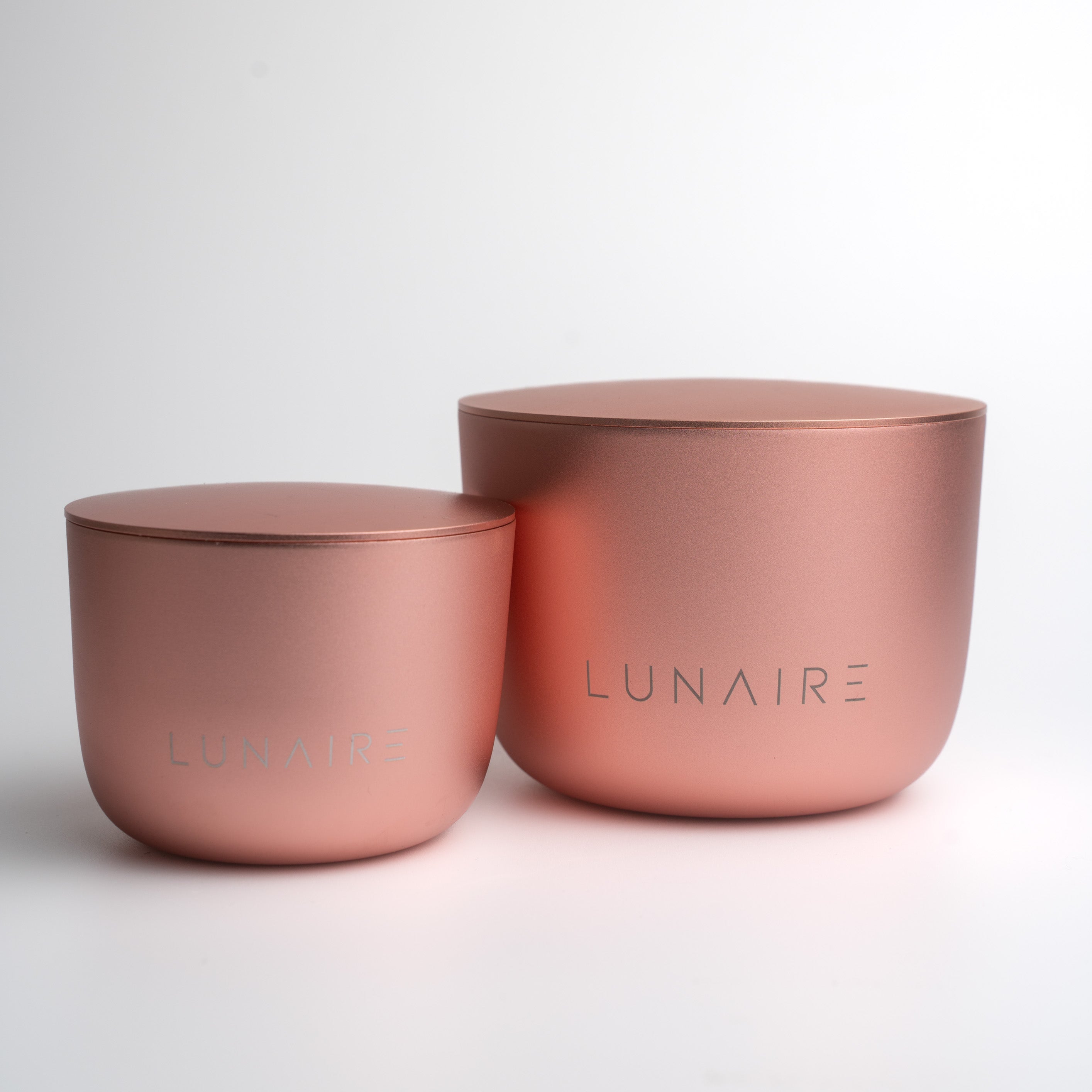 Two rose gold aluminium candle jars with 'LUNAIRE' branding on a white background