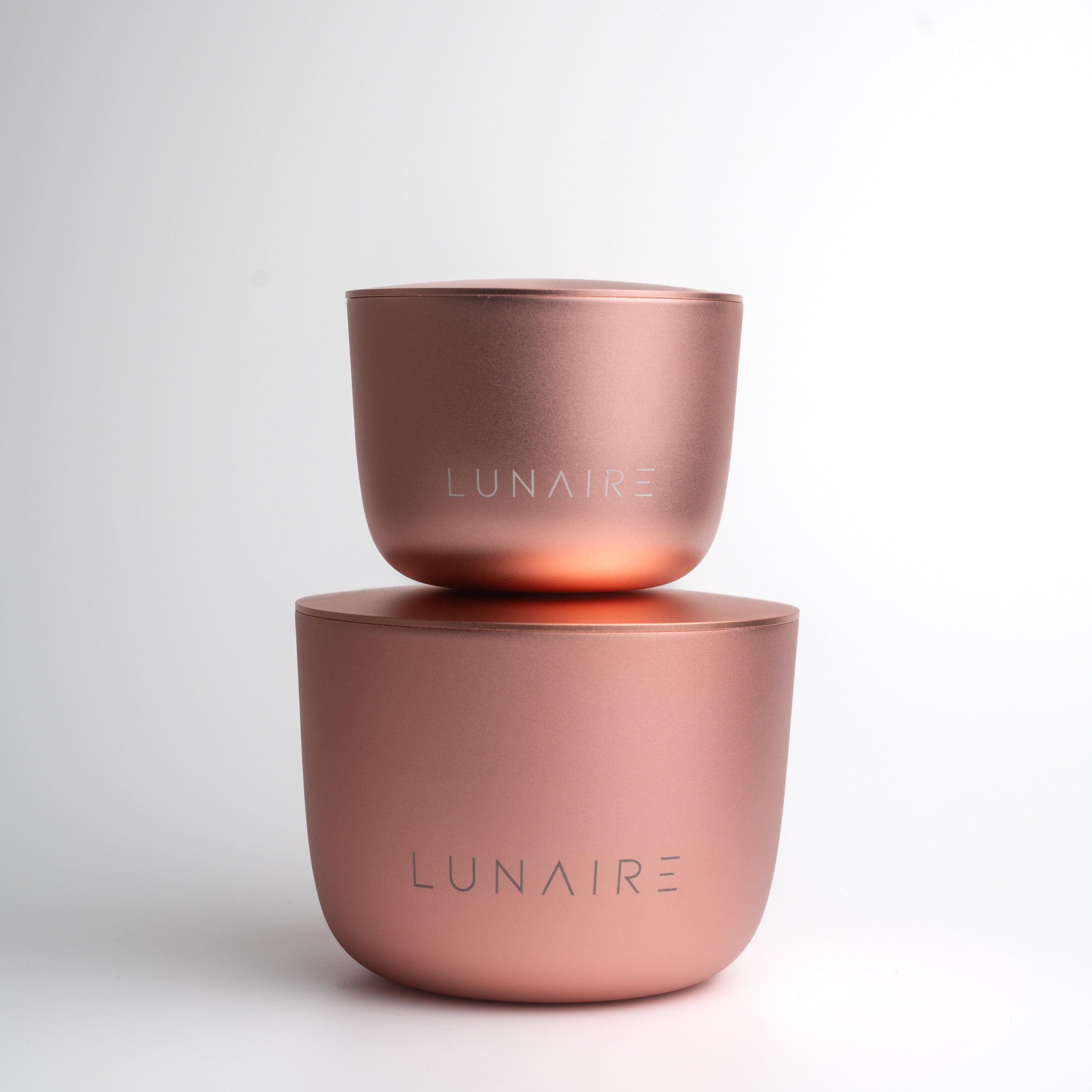 Two rose gold aluminium candle jars with 'LUNAIRE' branding on a light gray background