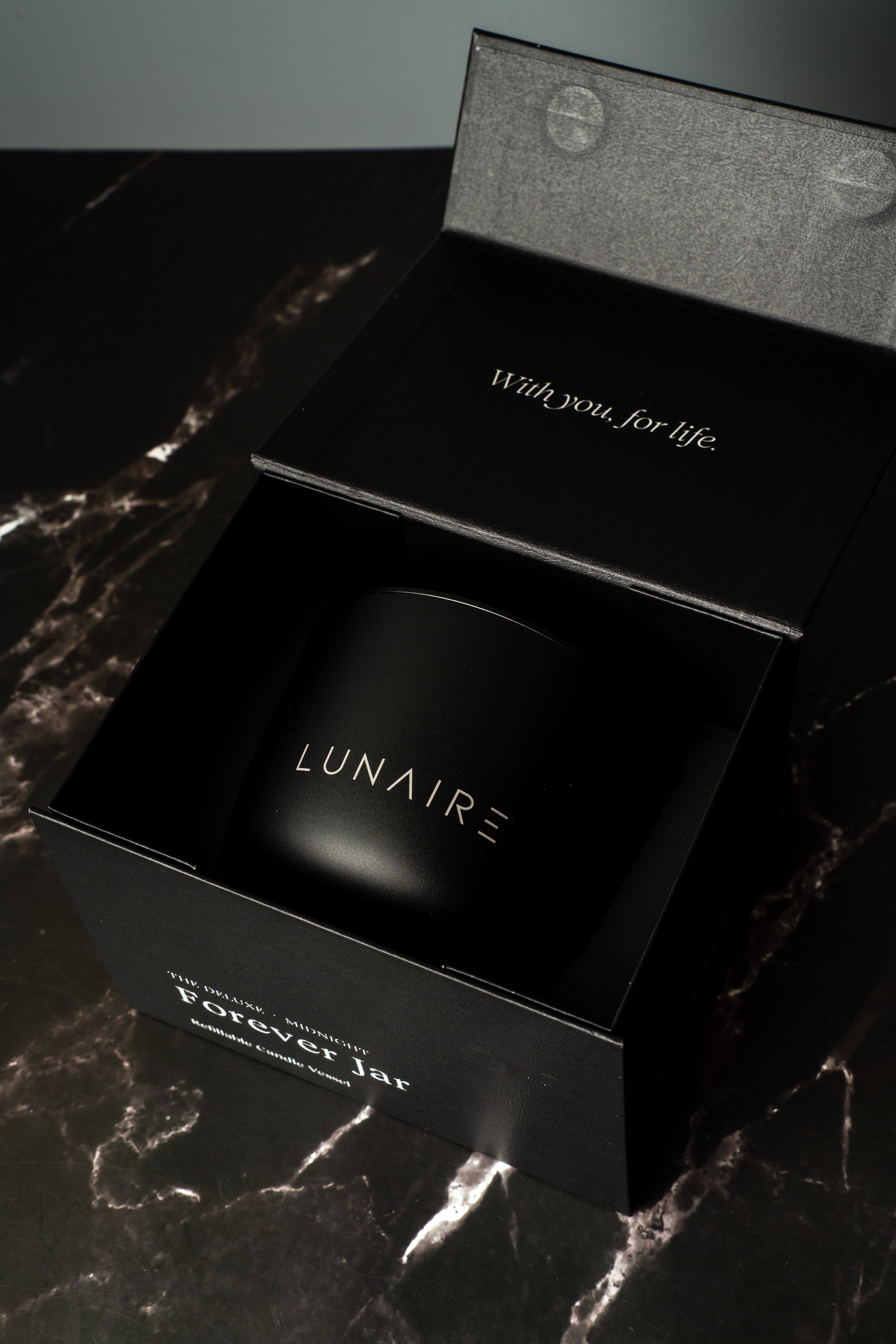 Black premium gift box with 'LUNAIRE' branding on a dark marble surface holding a refillable aluminium candle. 