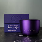 Purple candle jar with 'LUNAIRE' branding and a matching box on a dark surface.