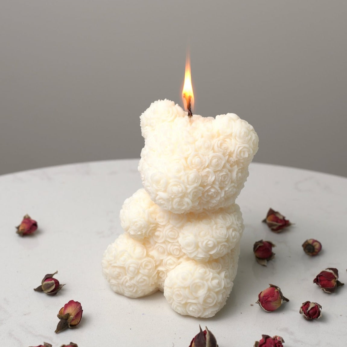 Bear Shaped Decorative Candle with intricate rose pattern lit on a surface covered in dried roses. 